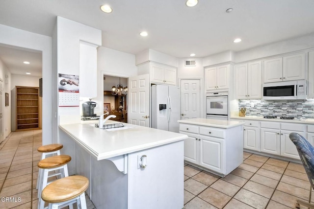 kitchen featuring white appliances, a breakfast bar area, white cabinetry, backsplash, and kitchen peninsula