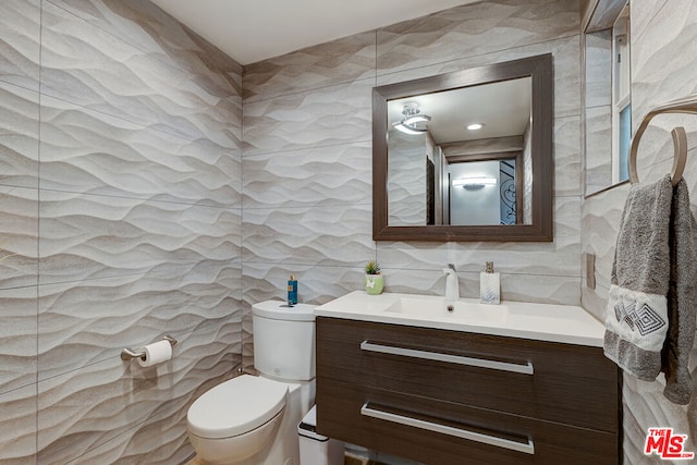 bathroom with toilet, tile walls, and vanity