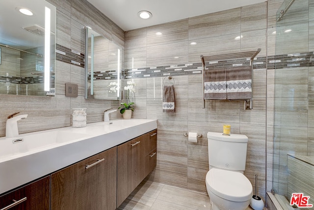 bathroom featuring toilet, vanity, tile walls, tile patterned flooring, and a shower with shower door