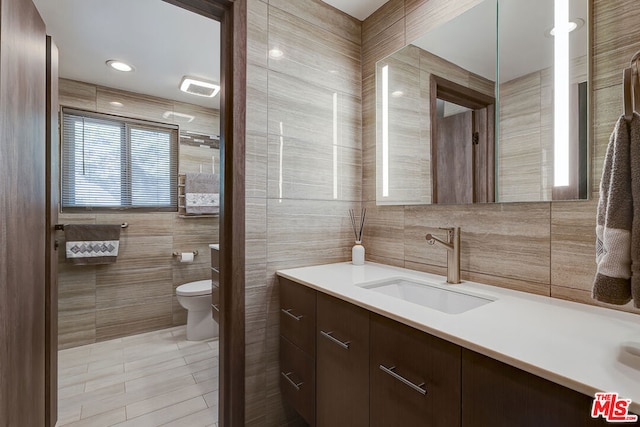 bathroom featuring toilet, vanity, tile walls, and tile patterned floors