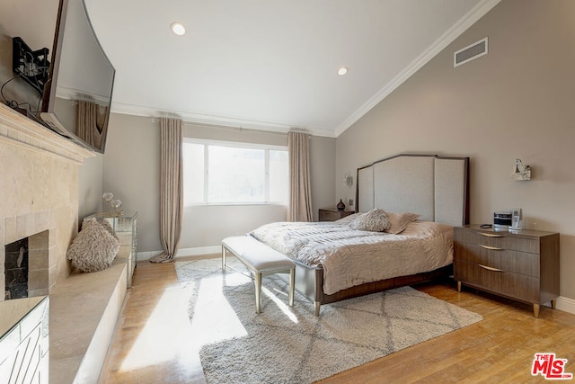 bedroom with light wood-type flooring, crown molding, lofted ceiling, and a tile fireplace