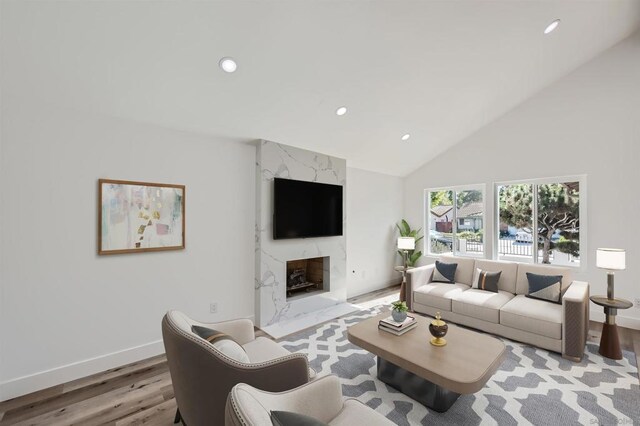 living room with high vaulted ceiling, light wood-type flooring, and a premium fireplace