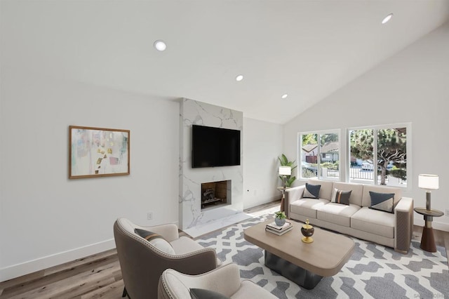 living room with light wood-type flooring, a premium fireplace, and high vaulted ceiling