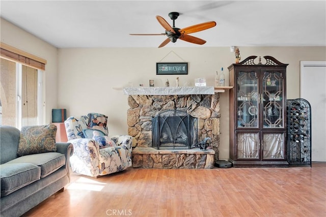 living room with ceiling fan, a stone fireplace, and hardwood / wood-style floors