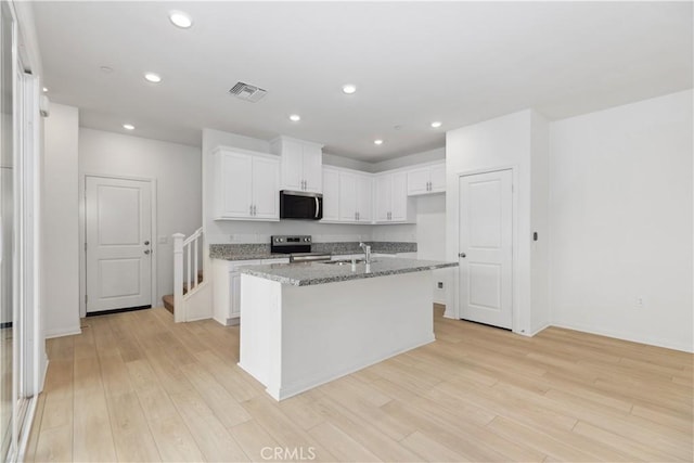 kitchen with white cabinetry, an island with sink, stainless steel appliances, light stone countertops, and sink