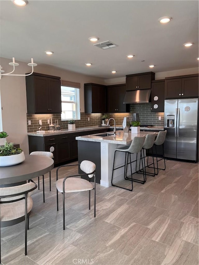 kitchen featuring sink, an island with sink, stainless steel fridge with ice dispenser, a kitchen breakfast bar, and dark brown cabinets