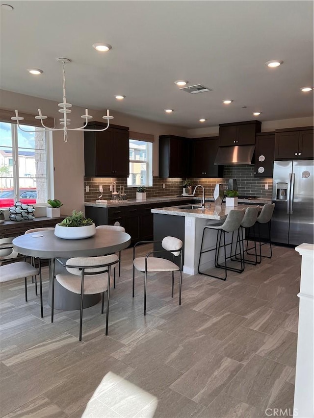 kitchen featuring dark brown cabinets, stainless steel fridge, plenty of natural light, and a center island with sink