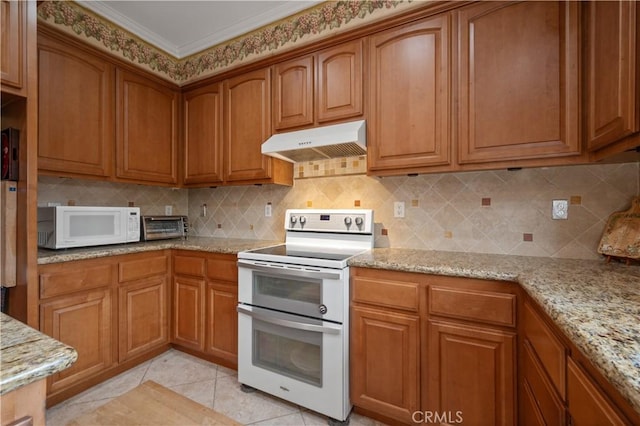 kitchen with white appliances, brown cabinets, light stone countertops, and under cabinet range hood