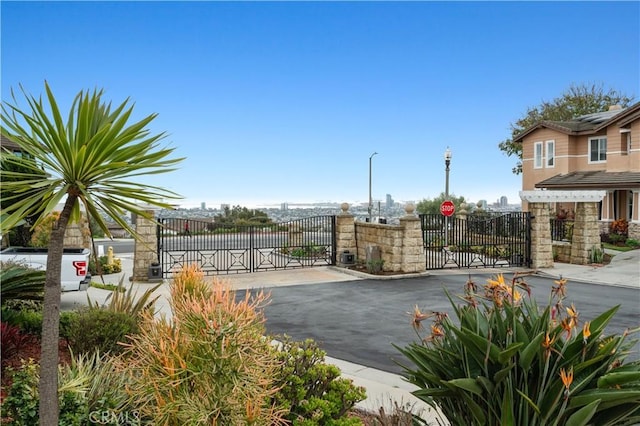 view of road featuring a gate, curbs, a gated entry, and street lights