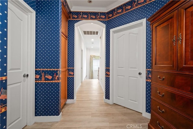 hall with wallpapered walls, light wood finished floors, visible vents, arched walkways, and ornamental molding