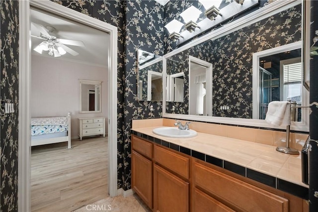 ensuite bathroom featuring ornamental molding, wood finished floors, vanity, and wallpapered walls