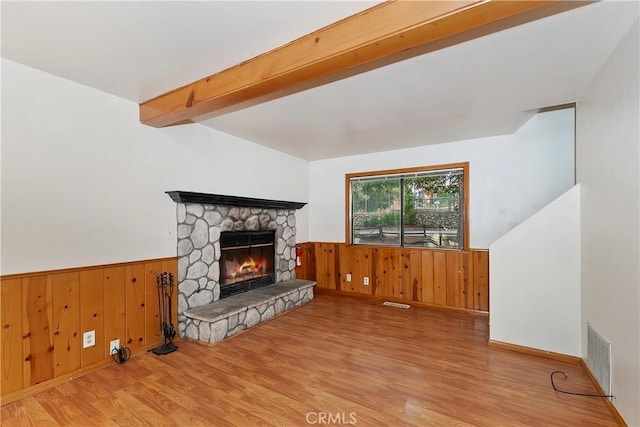 living room with light hardwood / wood-style flooring, beam ceiling, and a stone fireplace