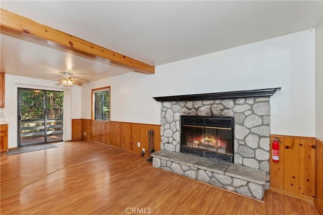 living room with hardwood / wood-style flooring, a stone fireplace, beamed ceiling, and ceiling fan