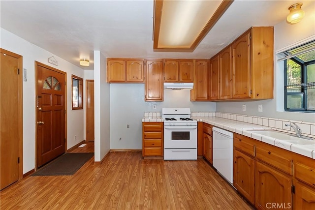 kitchen with sink, white appliances, tile countertops, and light wood-type flooring