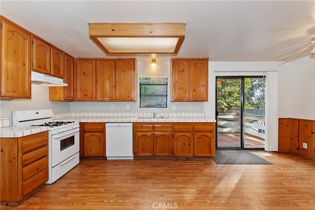 kitchen with white appliances, tile counters, wooden walls, sink, and light hardwood / wood-style flooring