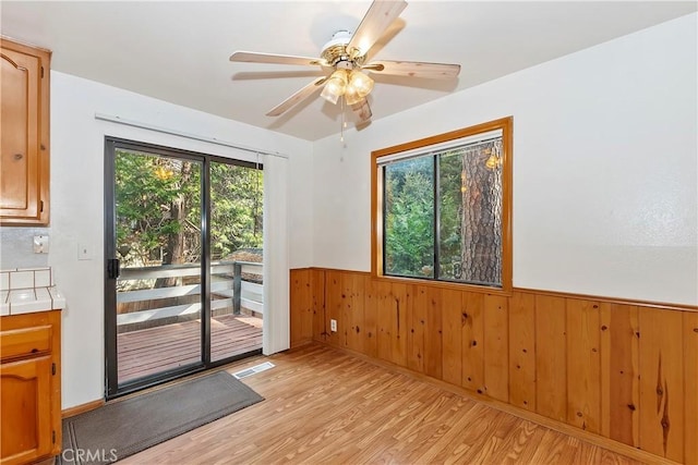 unfurnished room featuring ceiling fan, wood walls, and light wood-type flooring