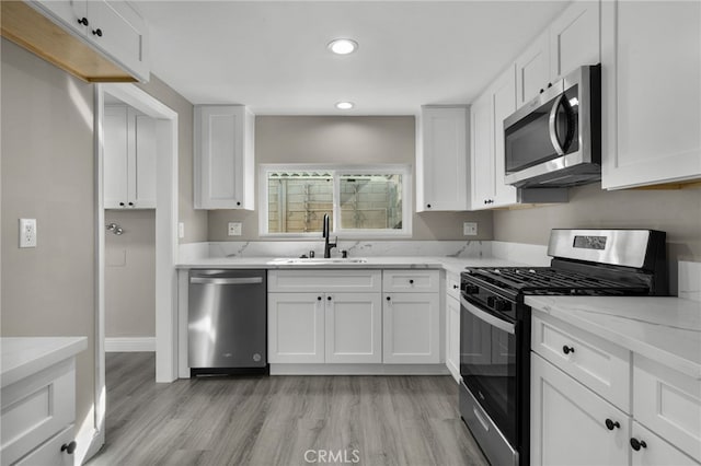 kitchen featuring light hardwood / wood-style floors, stainless steel appliances, white cabinets, light stone counters, and sink