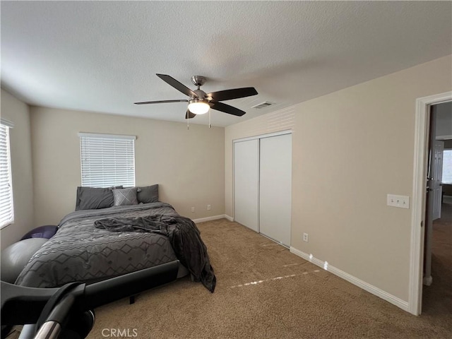 carpeted bedroom with a textured ceiling, ceiling fan, a closet, and multiple windows