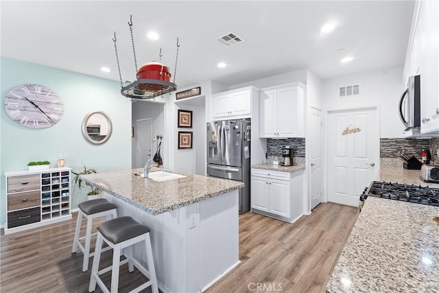 kitchen featuring appliances with stainless steel finishes, white cabinetry, an island with sink, tasteful backsplash, and light stone counters