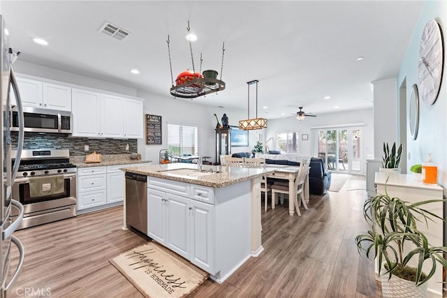 kitchen with ceiling fan, white cabinets, appliances with stainless steel finishes, and a kitchen island with sink