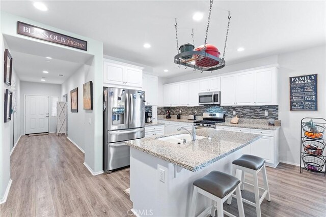 kitchen with a center island with sink, sink, white cabinetry, appliances with stainless steel finishes, and light stone counters