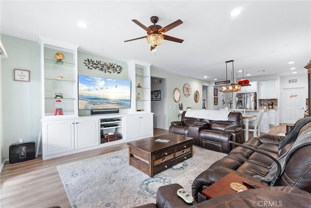 living room with ceiling fan, built in shelves, and light hardwood / wood-style flooring