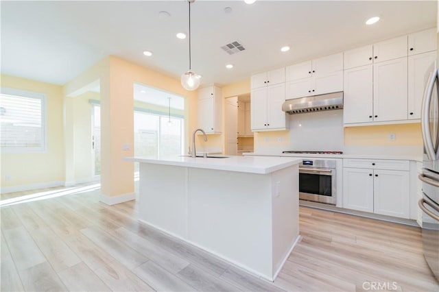 kitchen with pendant lighting, white cabinets, stainless steel appliances, sink, and a kitchen island with sink