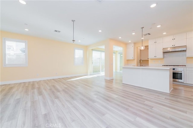 kitchen with pendant lighting, white cabinets, sink, oven, and light hardwood / wood-style flooring