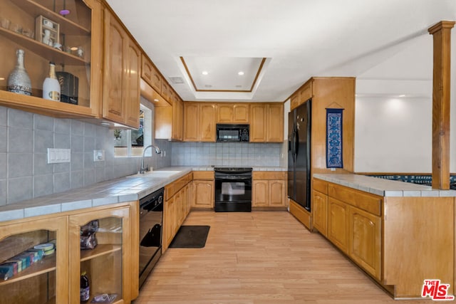 kitchen with tile counters, a raised ceiling, tasteful backsplash, black appliances, and sink