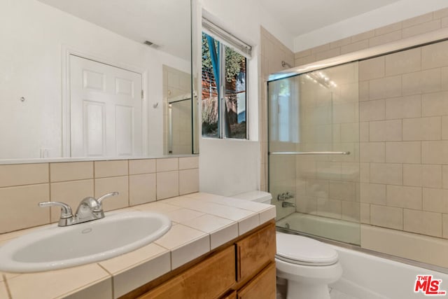 full bathroom featuring backsplash, combined bath / shower with glass door, vanity, and toilet