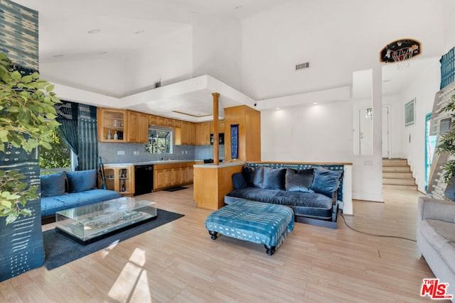 living room featuring light wood-type flooring, a towering ceiling, and sink