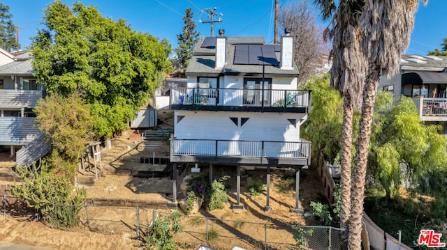 back of property with a balcony, a wooden deck, and solar panels