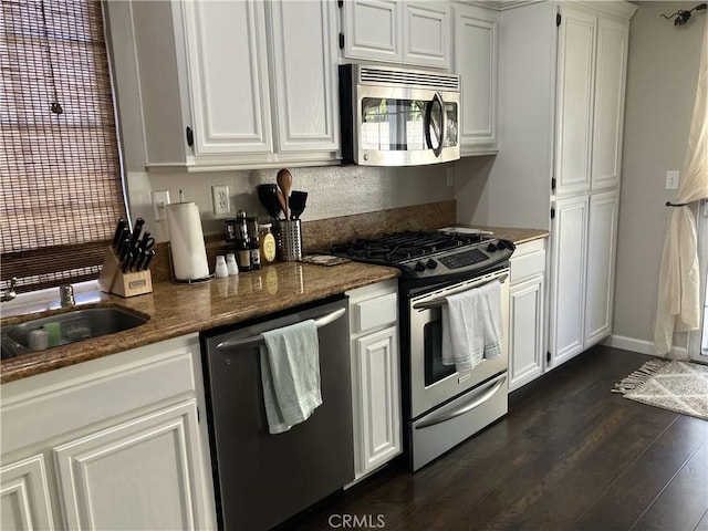 kitchen featuring sink, dark wood-type flooring, appliances with stainless steel finishes, white cabinets, and dark stone counters