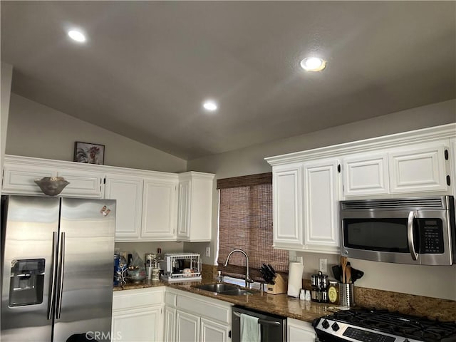 kitchen featuring appliances with stainless steel finishes, lofted ceiling, dark stone counters, white cabinets, and sink