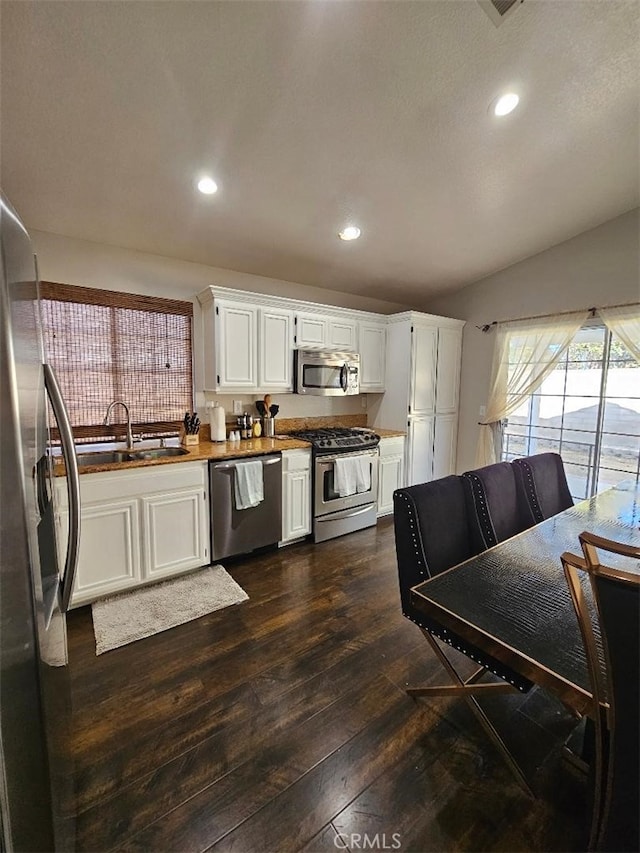 kitchen with appliances with stainless steel finishes, white cabinetry, dark hardwood / wood-style flooring, sink, and vaulted ceiling