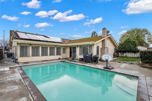 rear view of house with cooling unit, a patio, solar panels, and a fenced in pool