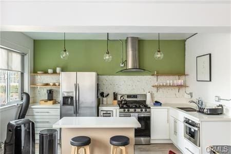 kitchen with white cabinetry, stainless steel appliances, wall chimney exhaust hood, and hanging light fixtures