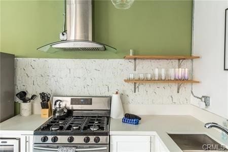 kitchen with exhaust hood, backsplash, sink, stainless steel range with gas stovetop, and white cabinetry