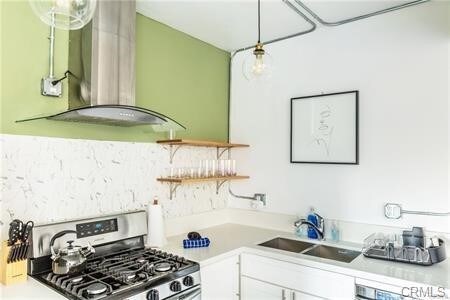 kitchen featuring decorative light fixtures, exhaust hood, sink, white cabinets, and stainless steel gas stove