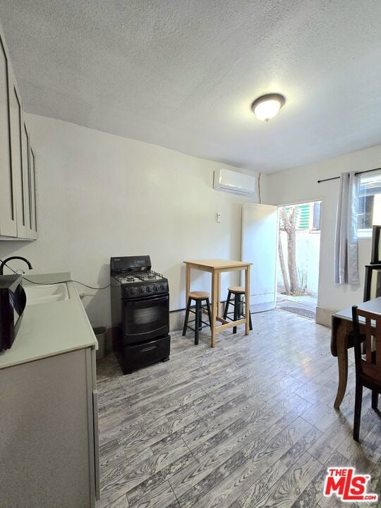 interior space with a textured ceiling, sink, light hardwood / wood-style floors, and a wall mounted air conditioner