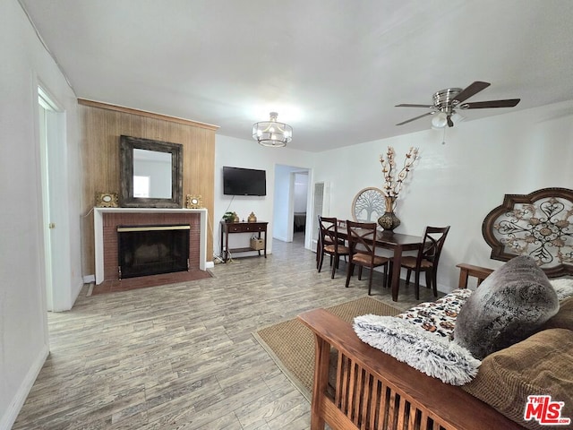 living room with a fireplace, ceiling fan with notable chandelier, and light hardwood / wood-style flooring