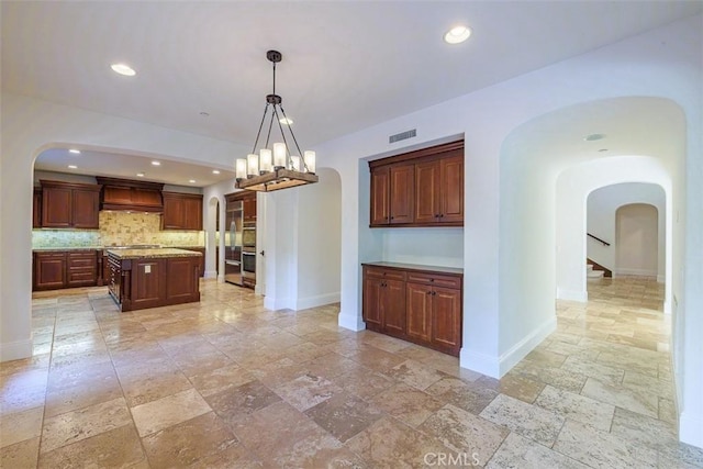 kitchen with pendant lighting, a center island, tasteful backsplash, an inviting chandelier, and premium range hood