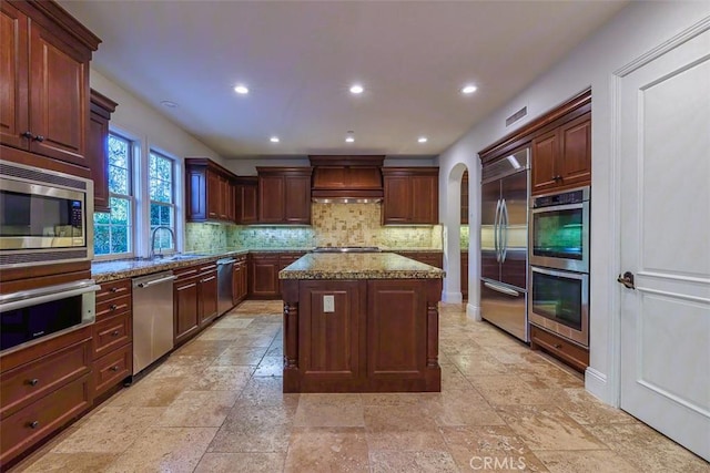 kitchen with backsplash, a center island, sink, built in appliances, and light stone countertops