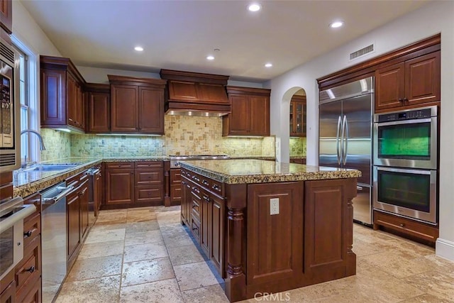 kitchen featuring appliances with stainless steel finishes, a center island, sink, backsplash, and light stone counters