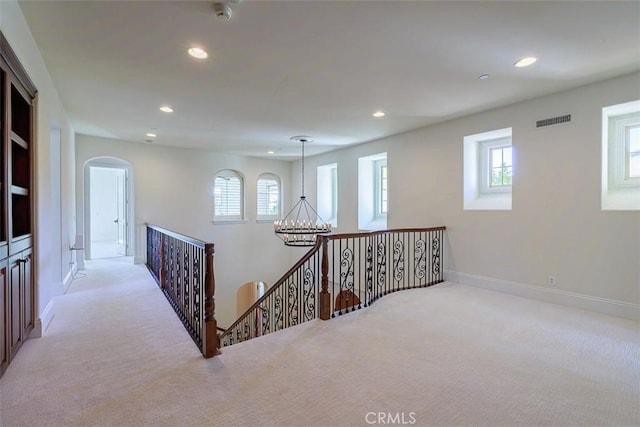 hall featuring light carpet, plenty of natural light, and a chandelier