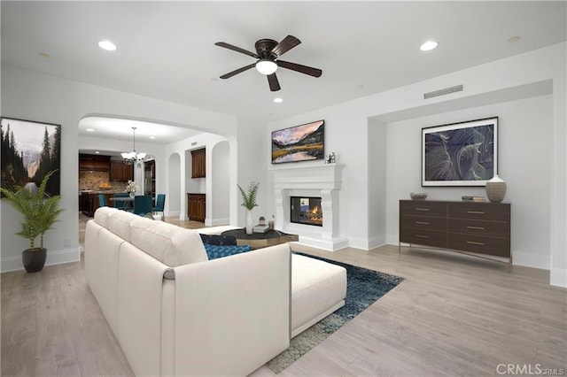 living room with ceiling fan with notable chandelier and light hardwood / wood-style floors