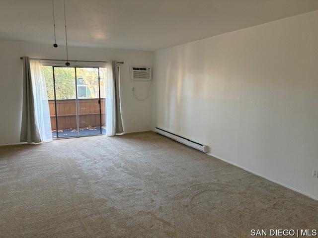 empty room with a baseboard heating unit, a wall unit AC, and carpet flooring