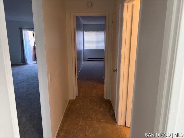 hall with dark carpet and a baseboard heating unit