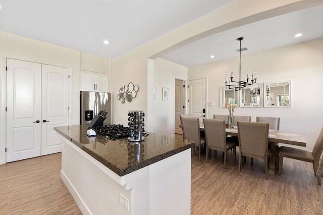 kitchen with decorative light fixtures, white cabinetry, stainless steel appliances, dark stone countertops, and light hardwood / wood-style floors