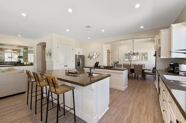 kitchen with pendant lighting, stainless steel refrigerator with ice dispenser, white cabinetry, a large island, and light wood-type flooring